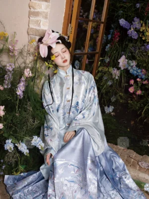 Light blue Ming Dynasty-inspired Hanfu outfit with standing collar top and flowing mamianqun skirt styled with floral hair accessories in a garden