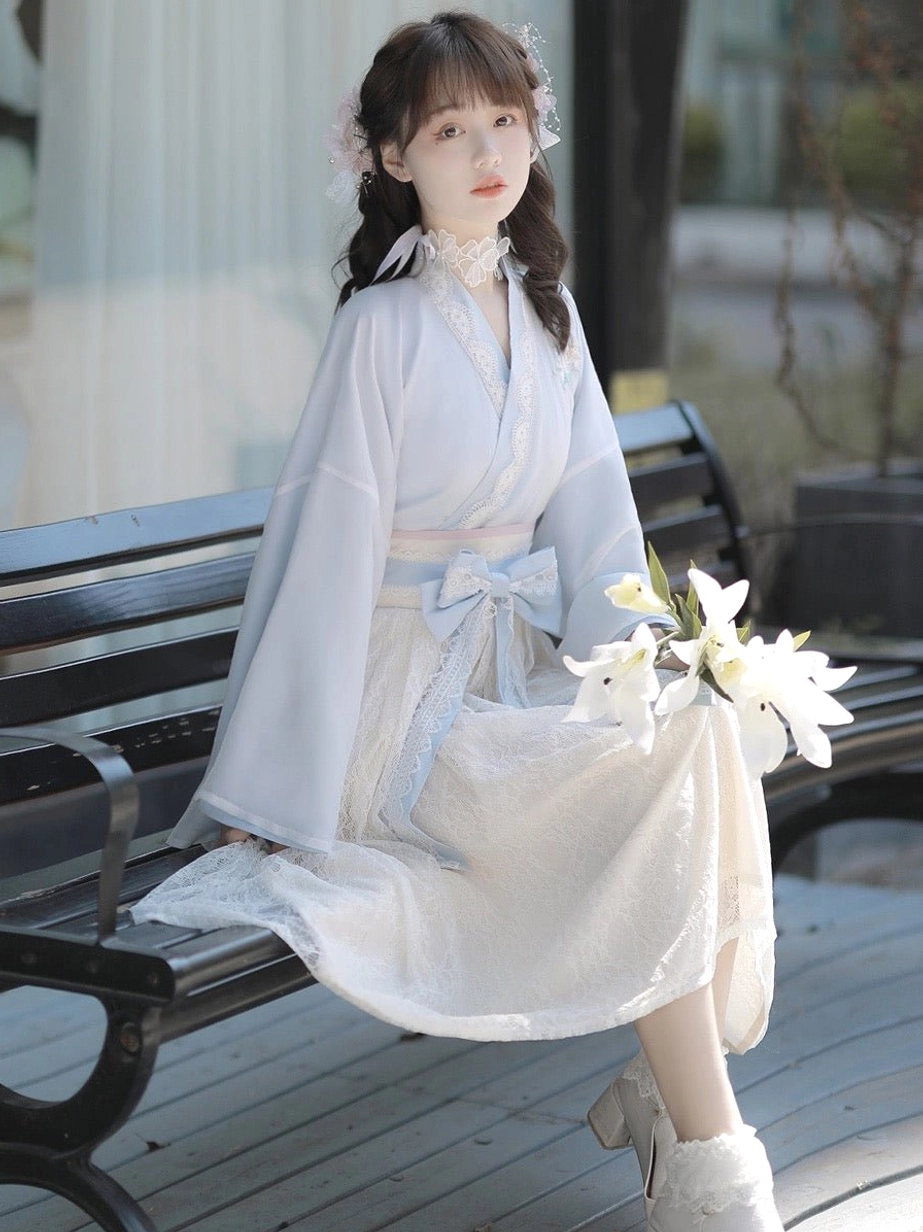 Light blue modern Chinese Hanfu dress seated view showing wide sleeves, lace-trimmed neckline, flowing skirt and waist bow
