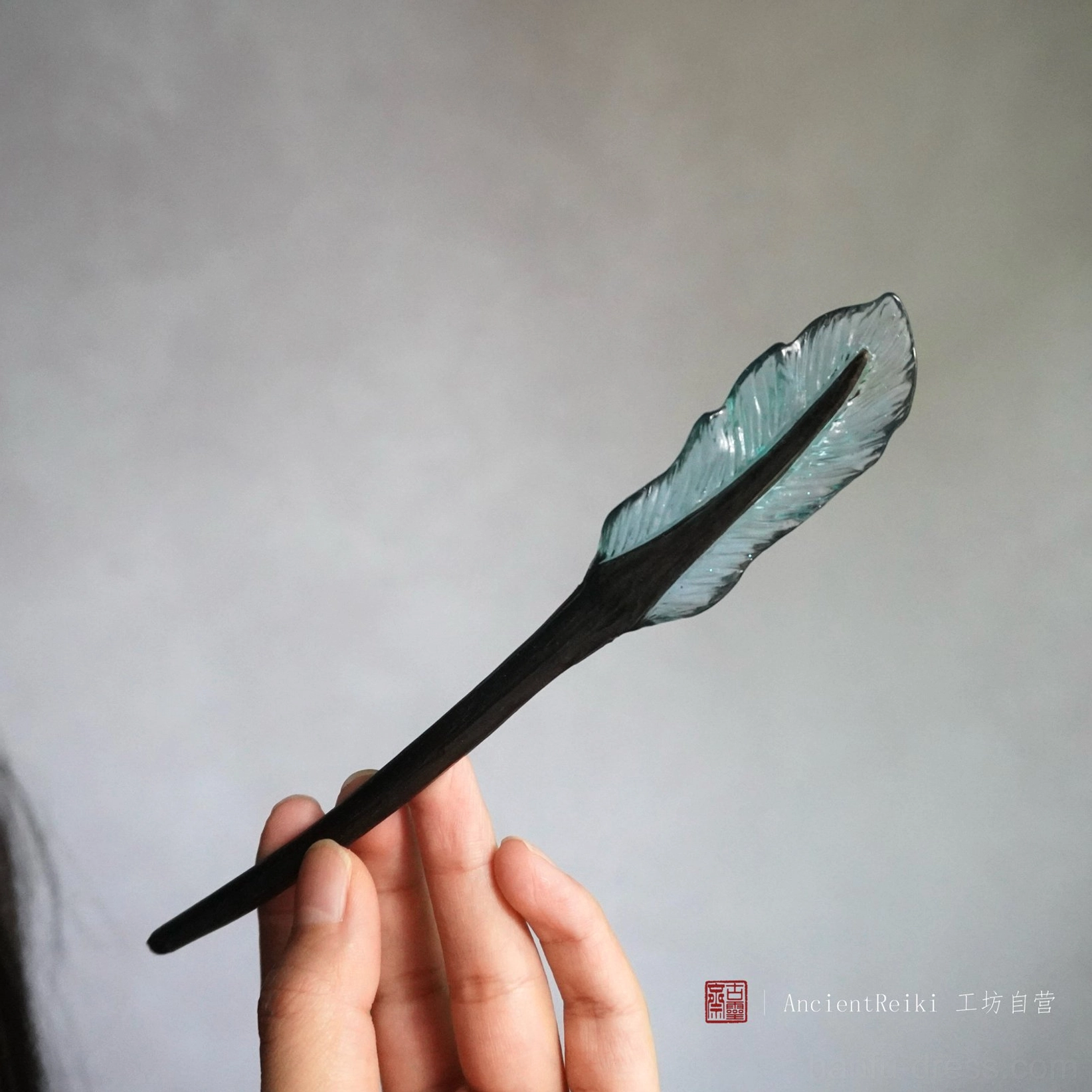 Light blue translucent feather Chinese hair stick held in hand, fantasy-inspired Hanfu hair accessory with black wooden shaft