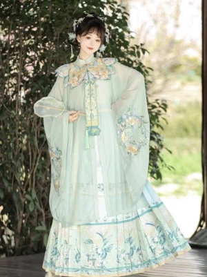 Light cyan Ming Dynasty summer Hanfu set with embroidered cloud collar, flowing wide sleeve robe, mamian skirt, floral embroidery, and front tassel pendant photographed in a traditional garden