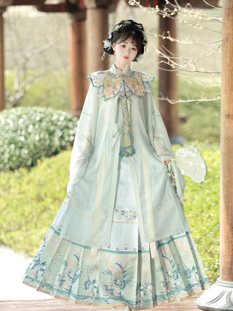Light cyan Ming Dynasty summer Hanfu ensemble with wide sleeves, embroidered collar, floral skirt hem, and round silk fan in an outdoor garden corridor