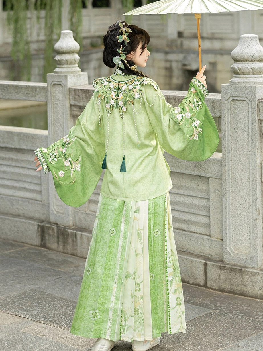 Back view of light green Ming Dynasty Hanfu set with embroidered cloud collar, tassel details and matching floral mamian skirt by a stone bridge