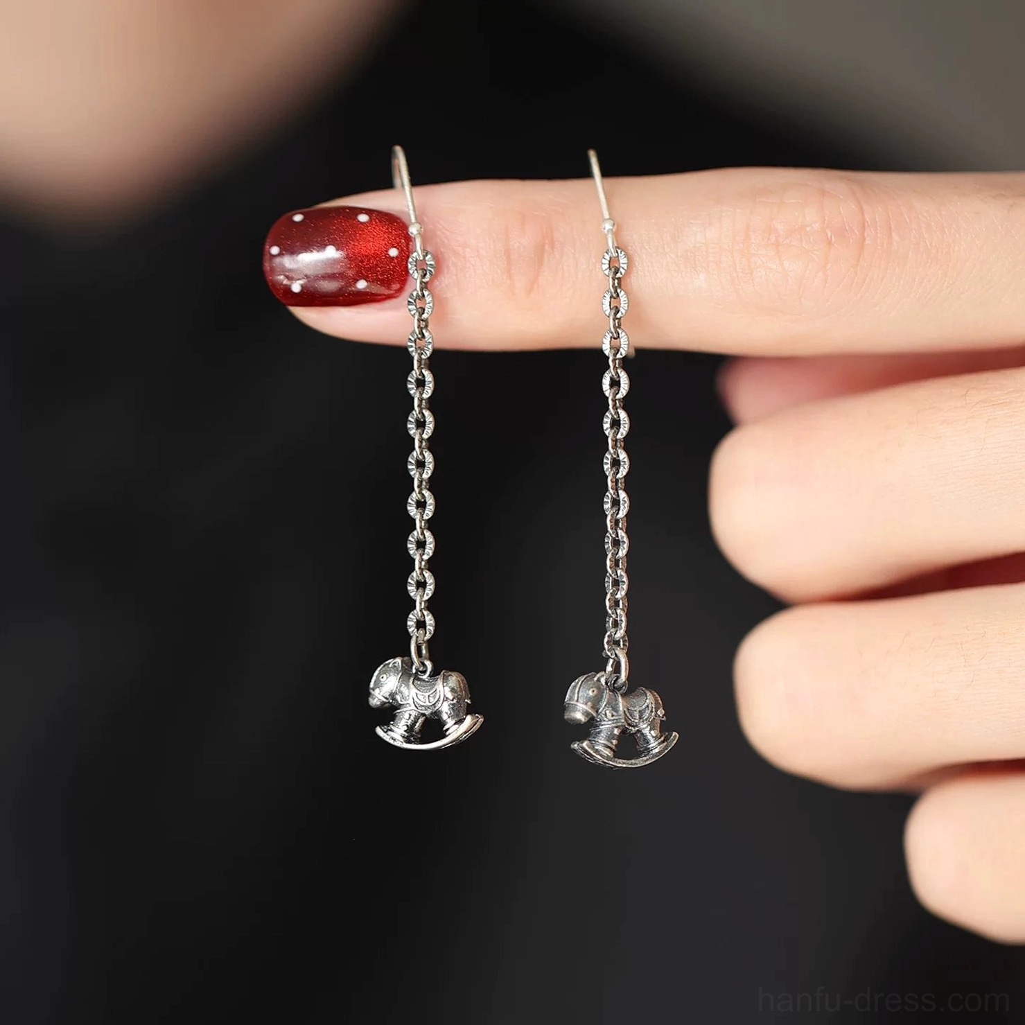 Close-up of lightweight silver rocking horse earrings held between fingers, showing detailed 3D pendants and polished metal finish