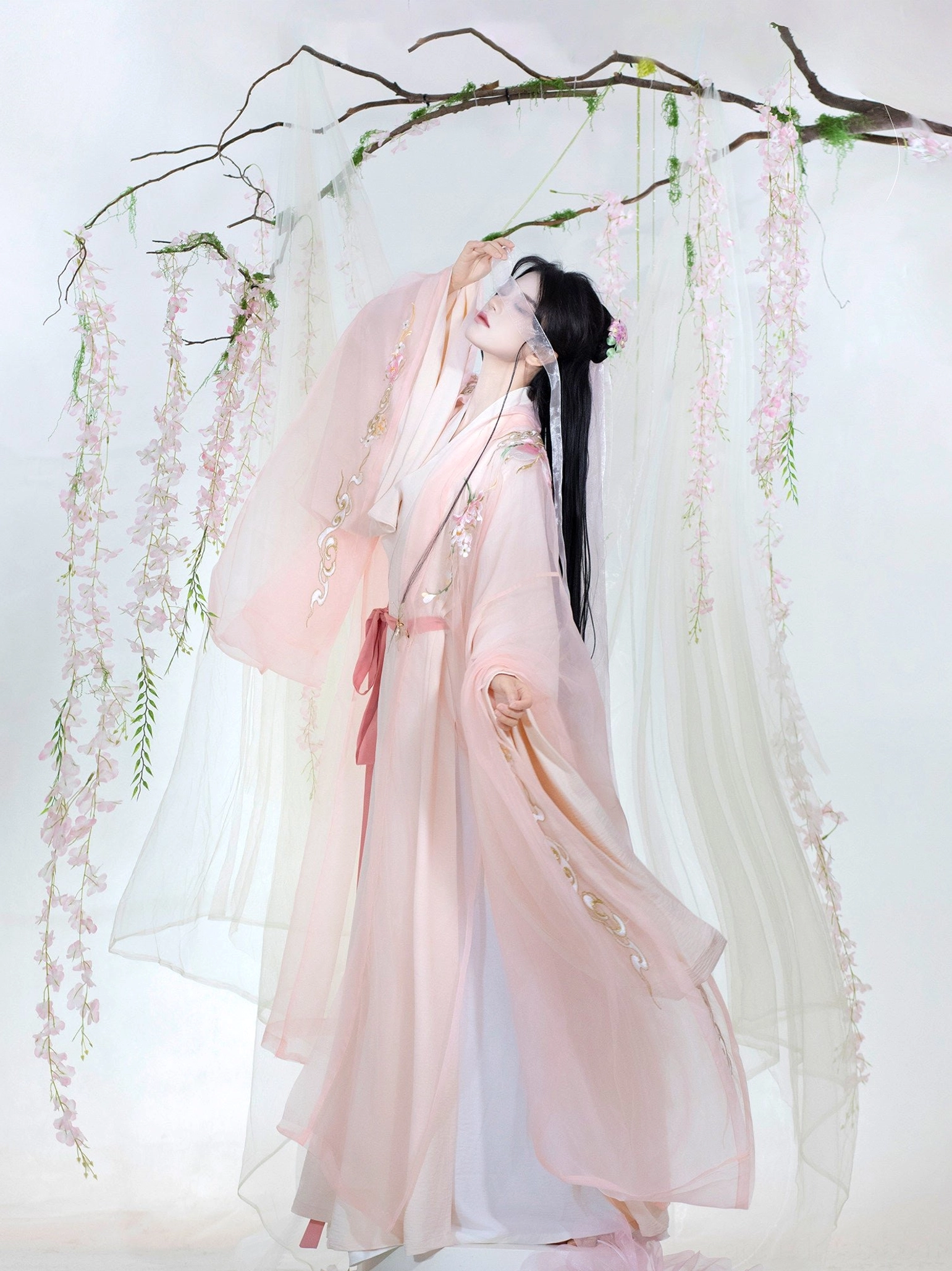 Low side view of a lightweight pink Xianxia hanfu costume with embroidered front panels, dramatic wide sleeves, matching waist sash, and flowing sheer fabric