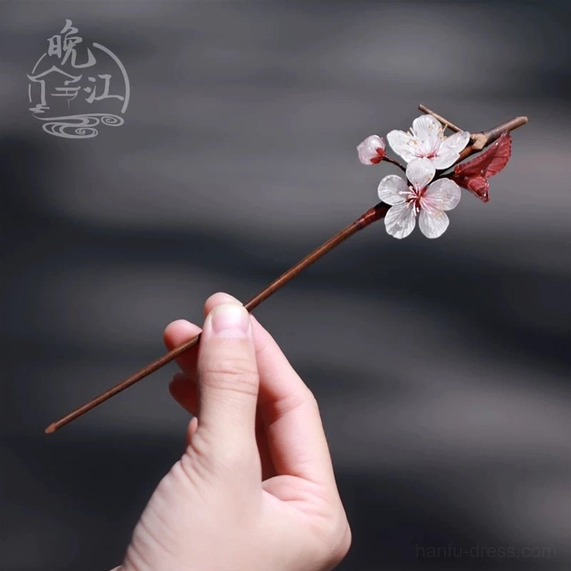 Single Lihua plum blossom Chinese hair stick held in hand to show scale, featuring a small white floral cluster, dark red leaves, and slim brown shaft