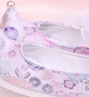 Close-up of lilac embroidered Chinese Hanfu shoes showing the floral brocade upper, pearl toe decoration, butterfly pearl collar ornament, white lining, and striped rubber outsole