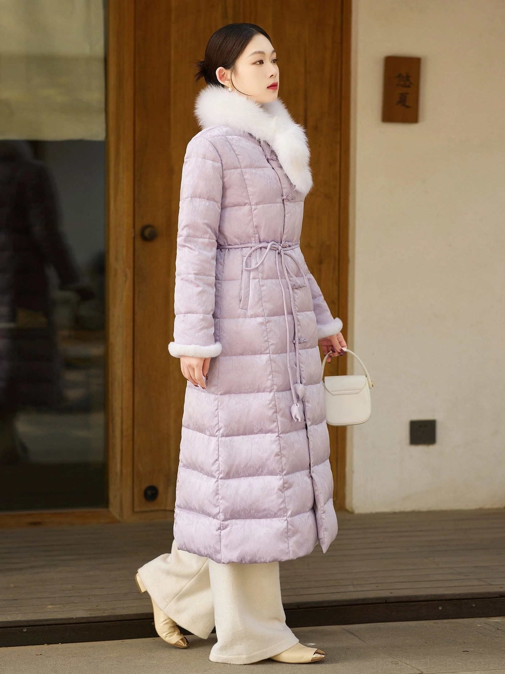 Left side view of a lilac women's Chinese-style winter down coat showing the long silhouette, fluffy fur trim, quilted texture and adjustable drawstring waist