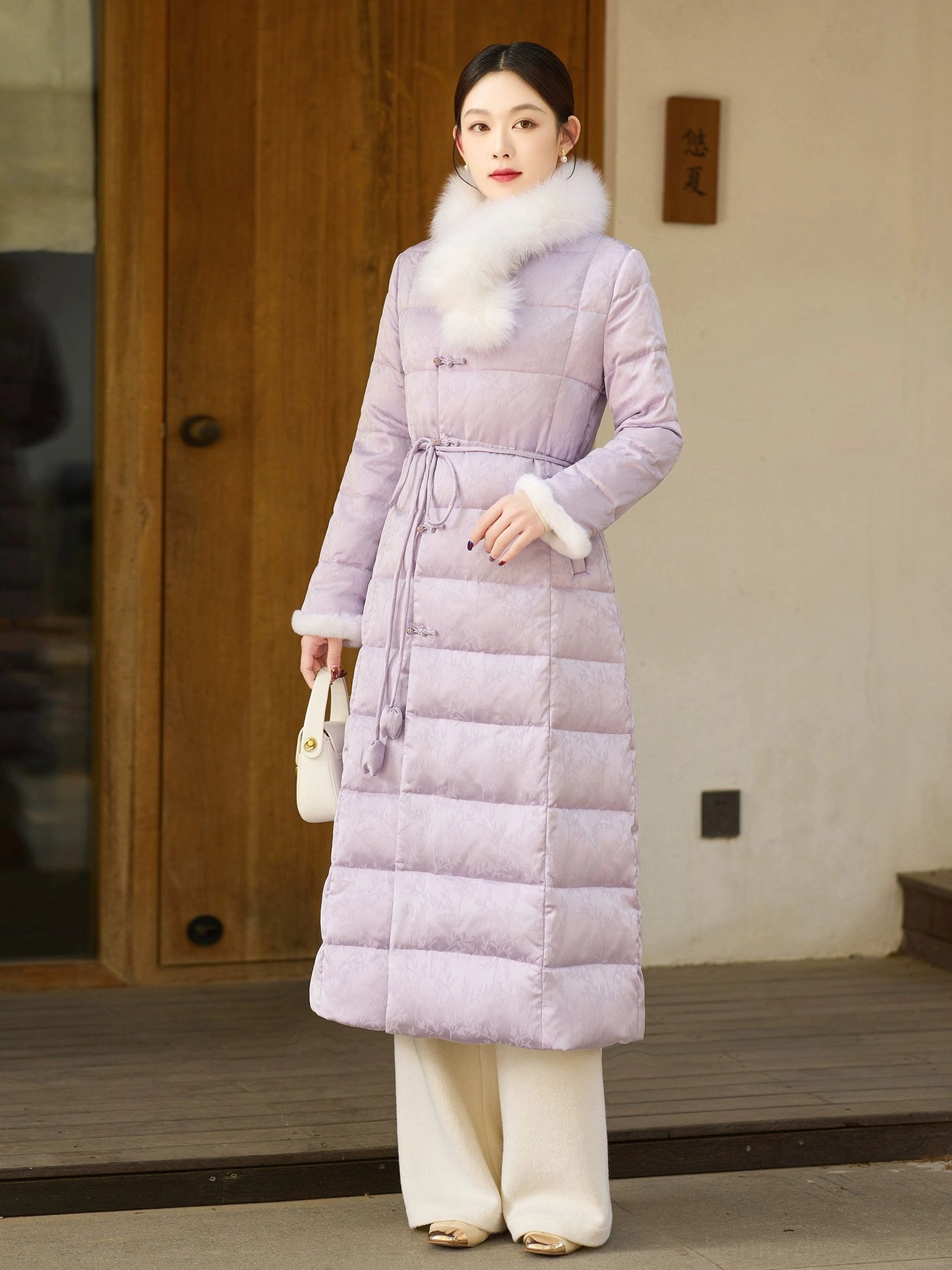 Full-body front view of a women's lilac qipao-inspired long down coat with white fur collar and cuffs, Chinese frog buttons, drawstring waist and quilted winter design