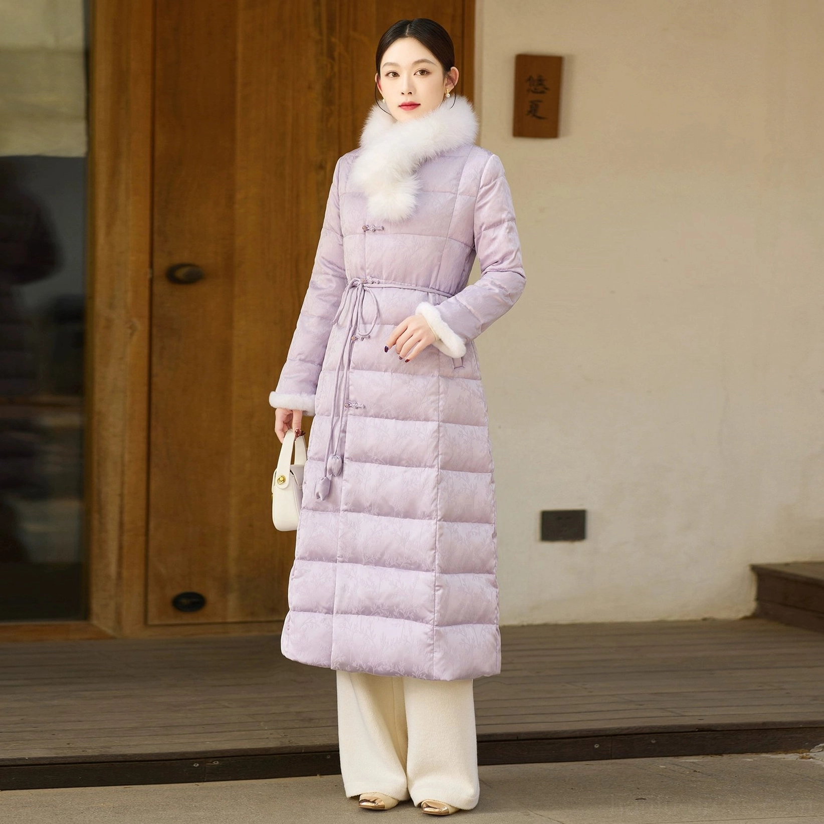 Right side full-body view of a women's lilac qipao-style long down coat with fur trim, frog buttons, quilted padding and decorative waist pendants