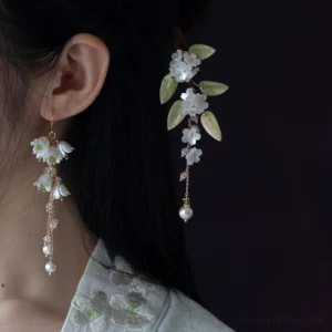 Close-up of lily of the valley Chinese earrings and retro floral earrings worn beside the ear with green leaves, flower charms, and pearl accents