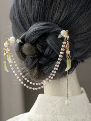 Lily of the valley Chinese Hanfu back hair pin with gold details pearl chains green flower charms and white hanging tassel worn on a braided chignon
