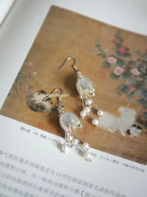 Silver hook lily of the valley Hanfu drop earrings with bell shaped filigree charms and white pearl tassels displayed on a traditional Chinese art book