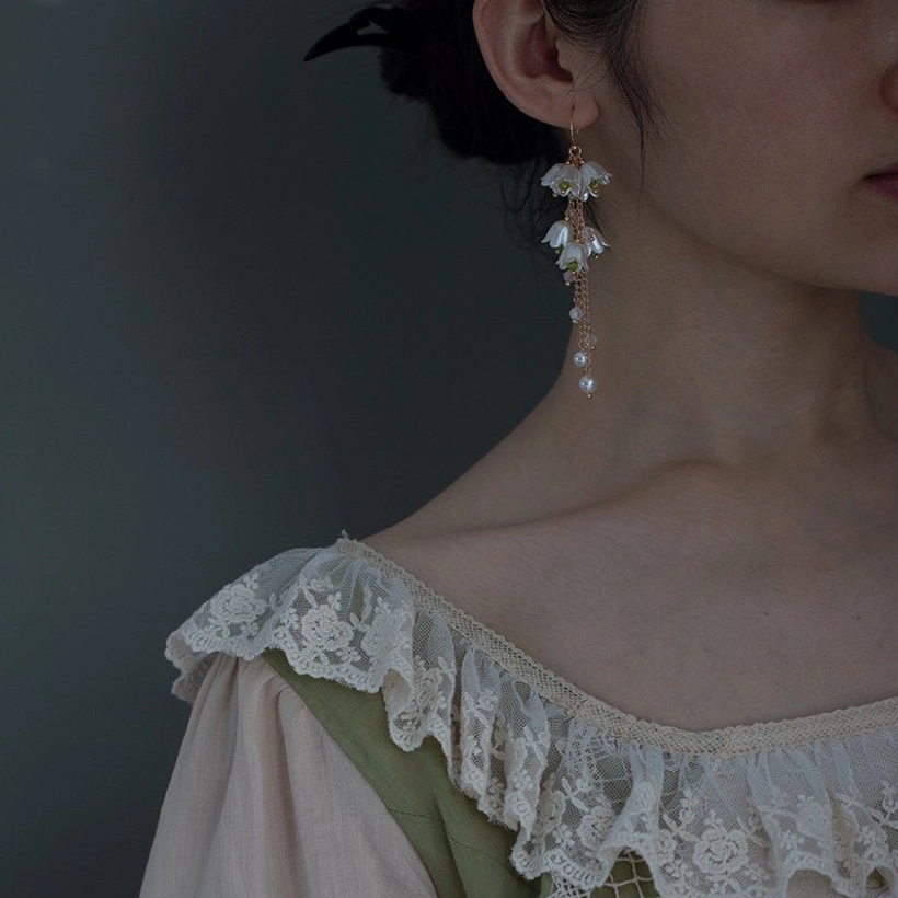 Profile view of lily of the valley Hanfu jewelry earrings with slim gold tassel chains, bell flowers, beads, and subtle pearl decorations