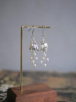 Lily of the valley pearl tassel Chinese earrings displayed on a brass wooden jewelry stand, featuring silver toned filigree flower pendants for Hanfu styling