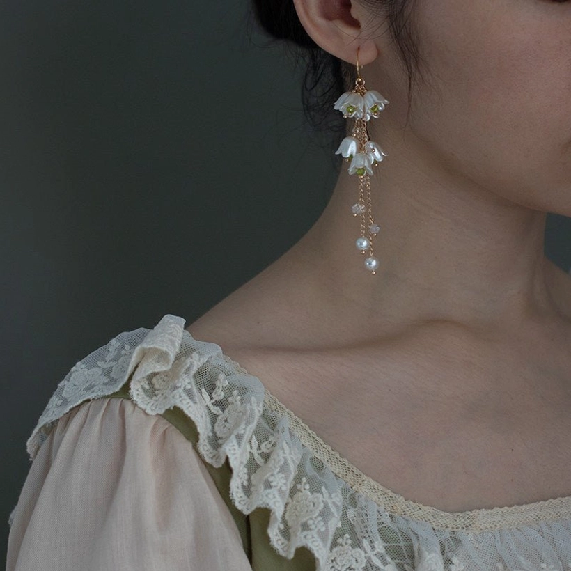 Lily of the valley tassel drop earrings worn with a vintage blouse, featuring delicate white flower clusters, gold chains, beads, and pearl pendants