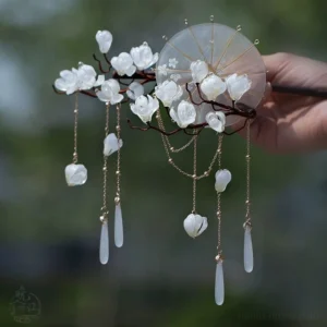 Lily and umbrella Chinese hair stick with white resin flowers gold chains and layered tassels displayed against a soft green outdoor background