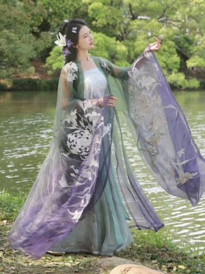 Lily of the valley embroidered Tang Dynasty hanfu set with sheer wide sleeves, gradient green and purple cardigan, camisole, and flowing qiyao ruqun skirt shown in a lakeside garden