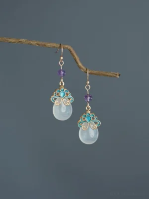 Lingluo blue enamel jade-tone Chinese drop earrings with purple beads and gold-tone comfort clip-on closure displayed on a dry branch