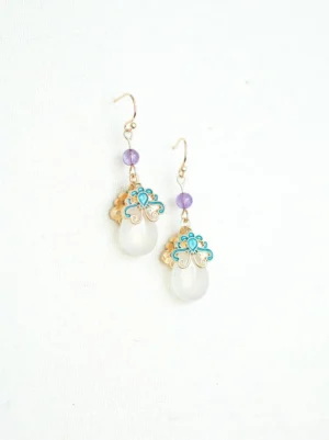 Vintage Chinese style blue enamel drop earrings with purple round beads, gold ear wires, and smooth white jade-tone teardrop pendants on ivory fabric