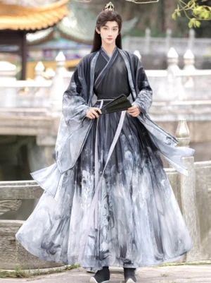 Male model wearing black and grey ink-wash Xianxia hanfu set with dragon print, wide sleeves, lavender waist sash and black folding fan in a traditional Chinese garden