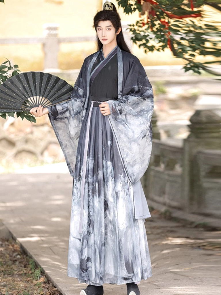 Three-quarter view of male model in black and grey Chinese fantasy Xianxia hanfu set holding a black folding fan with wide flowing sleeves