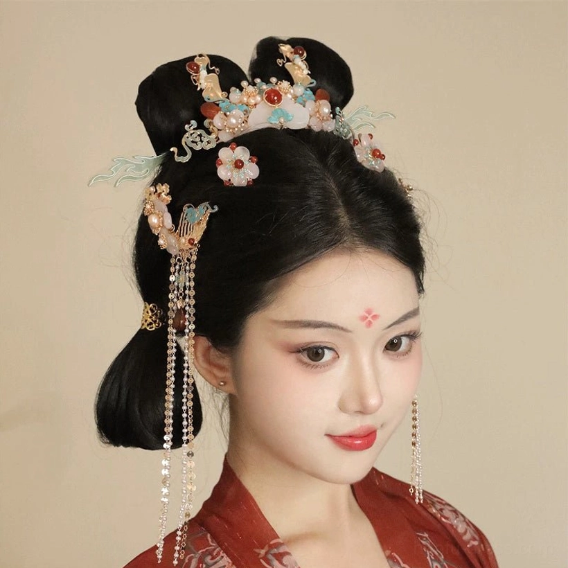 Model wearing coordinated Chinese Hanfu hair ornaments with a double traditional bun, floral face makeup, temple tassels, and a matching decorative crown