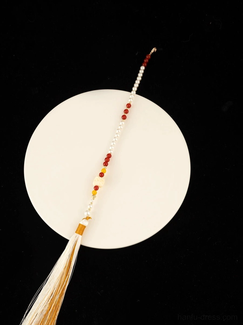 Single long Chinese necklace tassel accessory with white red and amber beads and a neat beige silk tassel displayed on a white porcelain plate