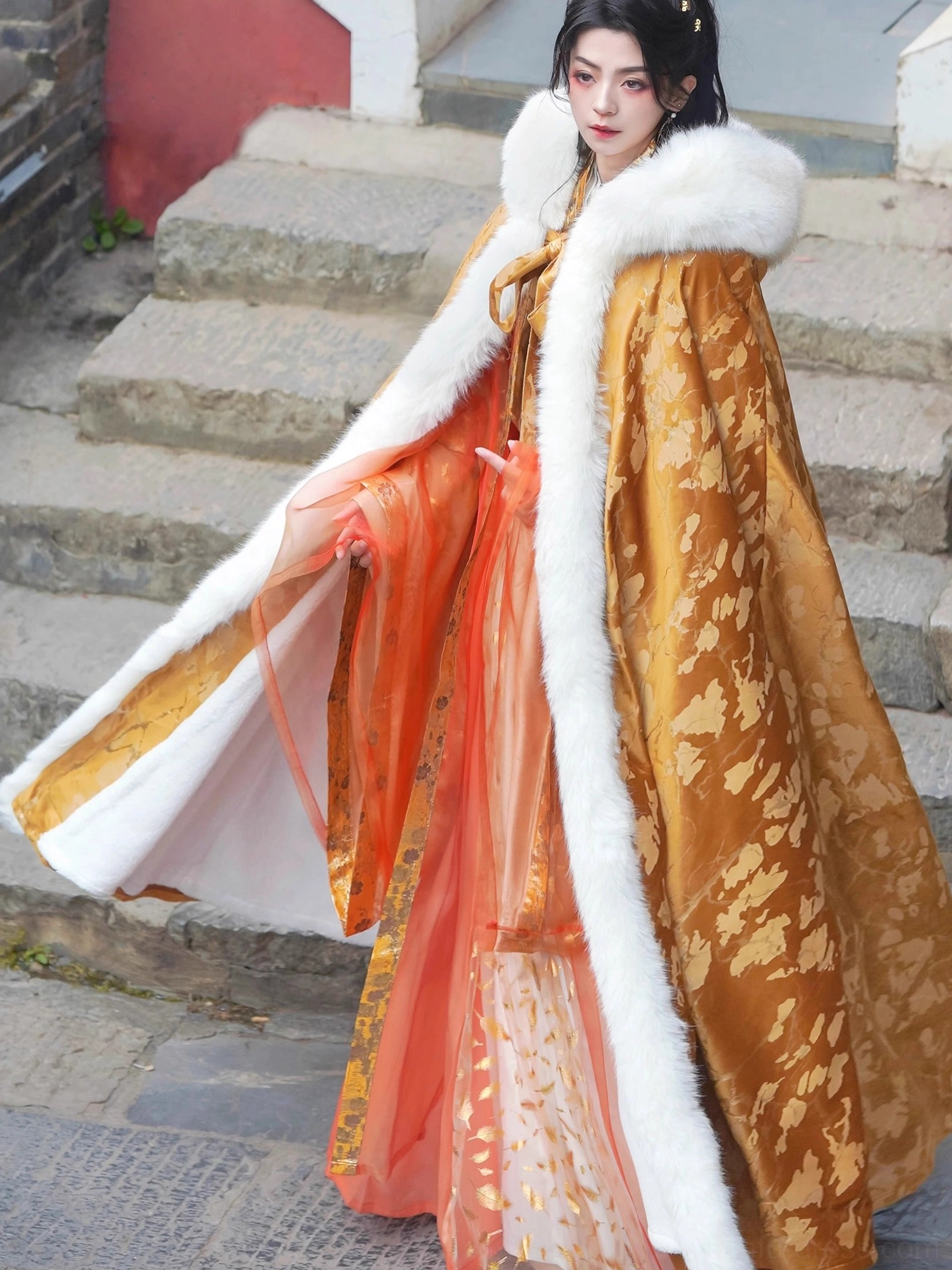 Side three-quarter view of a long floor-length Hanfu cloak with white faux fur trim, flowing train, and gold embossed fabric inspired by Chinese historical fashion