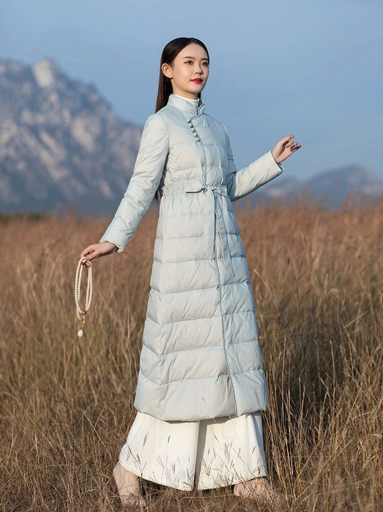 Three quarter view of a long Hanfu inspired winter down coat for women in pale blue with traditional frog fastenings detachable waist belt and elegant stand collar