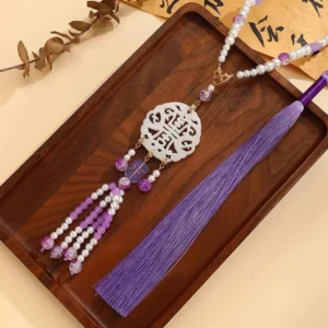 Long purple tassel Chinese necklace shown from an angled overhead view with a hollow Shou longevity pendant, purple white beaded chain, and decorative tassel
