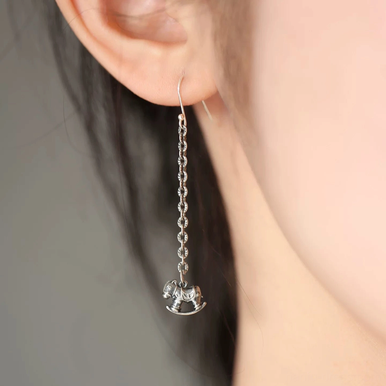 Side view of a long silver-toned rocking horse earring worn near the ear and neck, styled as an elegant everyday dangle accessory