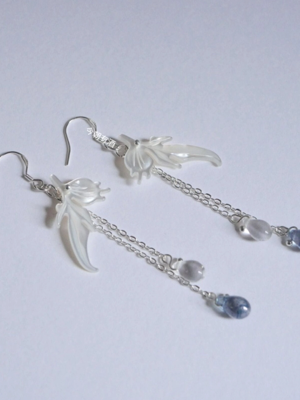 Long tassel goldfish Hanfu earrings with shell-like white fish pendants, silver chains, light gray beads, and dark blue teardrop accessories shown in a flat lay