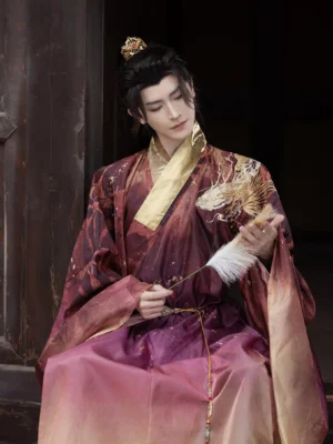 Long Yin Ming-inspired Taoist hanfu robe for men with burgundy to pale yellow ombre fabric, golden dragon shoulder embroidery, wide sleeves, cross collar, and male model holding a feather fan in a traditional Chinese courtyard