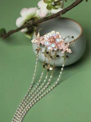 Lotus Fragrance Hanfu hair pin with pink iridescent flower, gold-tone butterfly accents, pearl chains, and sequin tassels displayed on a blue Chinese porcelain bowl