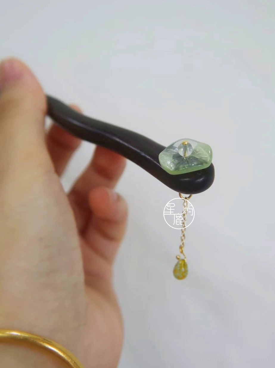 Side view of lotus inspired Chinese hair stick held in hand, showing wavy wooden body, pale green stone ornament, and teardrop tassel pendant