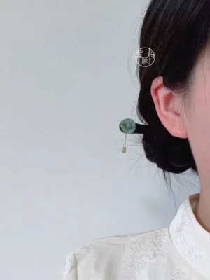 Lotus leaf Chinese hair stick worn in a coiled bun, featuring a dark brown wavy wooden design, jade-green stone detail, and gold tassel pendant