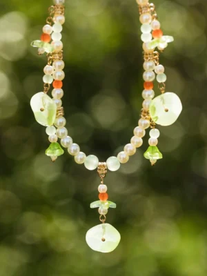 Close-up of a Chinese style lotus leaf statement necklace with layered pearl strands, green lotus pendant, red orange accent beads, and gold toned hardware