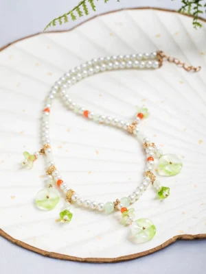 Lotus leaf freshwater pearl Chinese style necklace displayed on a vintage fan tray with green botanical charms, orange red agate beads, and gold toned details