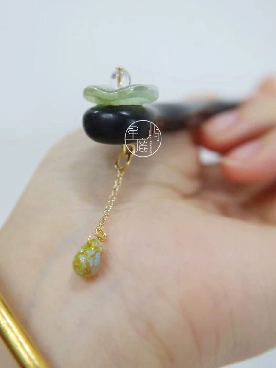Close-up detail of jade-green stone and gold teardrop tassel on a dark brown lotus leaf Hanfu hair stick