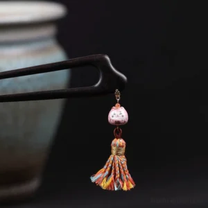 Close-up side view of lucky cat Chinese hair stick with dark ebony-toned wooden pin, pink cat pendant, gold-tone detail, and bright multicolor tassel
