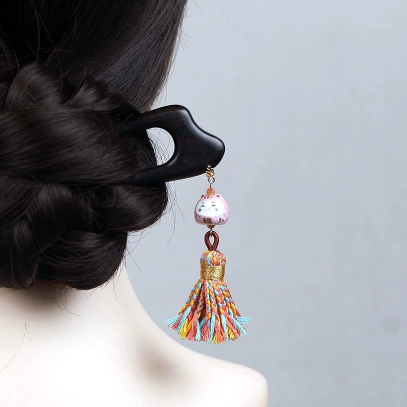 Lucky cat tassel Chinese hair stick worn in a traditional Hanfu coiled hairstyle, featuring a dark wooden double-pronged pin, pink cat charm, and colorful tassel