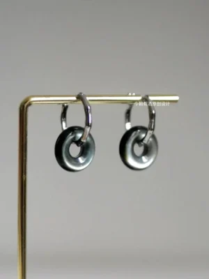 Lucky Loop Chinese hoop earrings displayed on a golden stand, showing the hollow circular pendant with glossy black and silver gradient finish and lever-back clasp