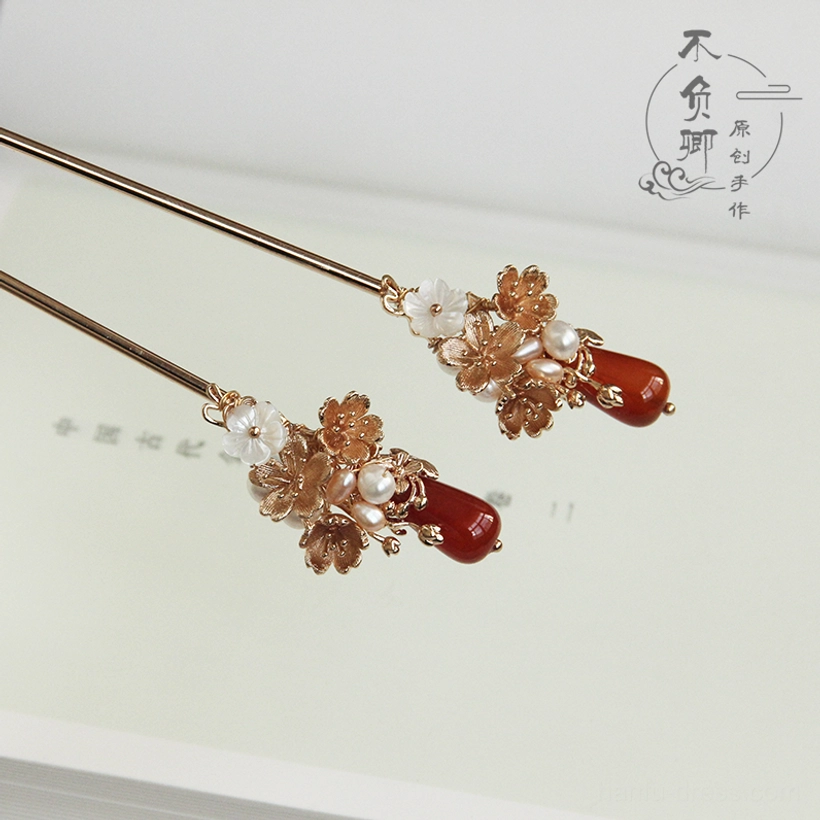 Side view of Luoshen ancient Chinese hairpins with warm metal shafts, amber gold floral ornaments, and red agate-style finials on vintage book pages