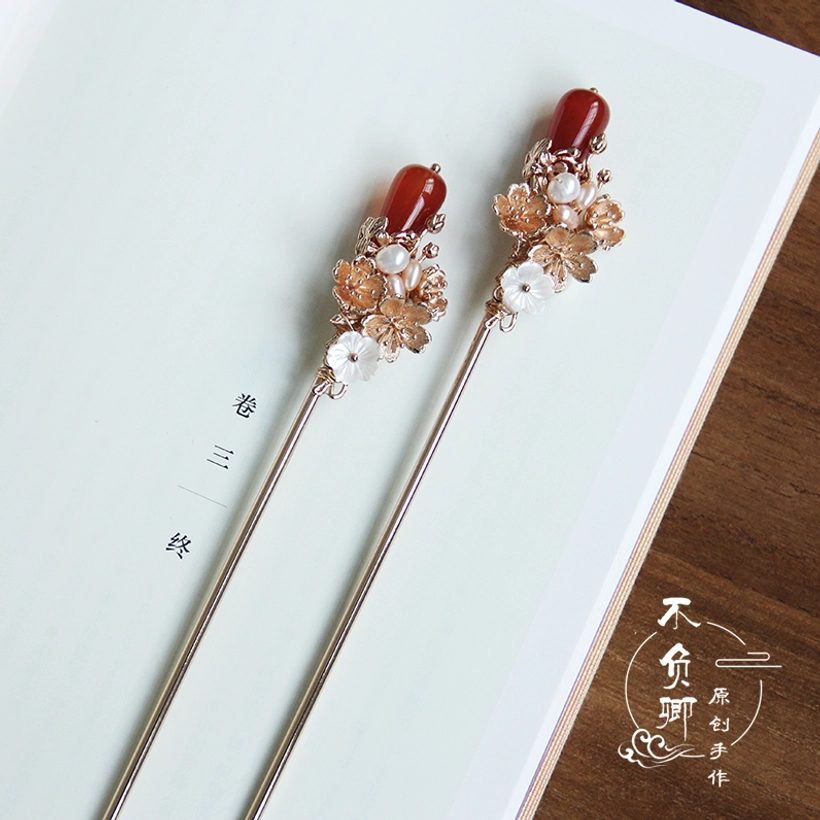 Traditional Chinese floral hair sticks displayed on an open book with matching red agate-style pendants, gold flower clusters, and white pearl details
