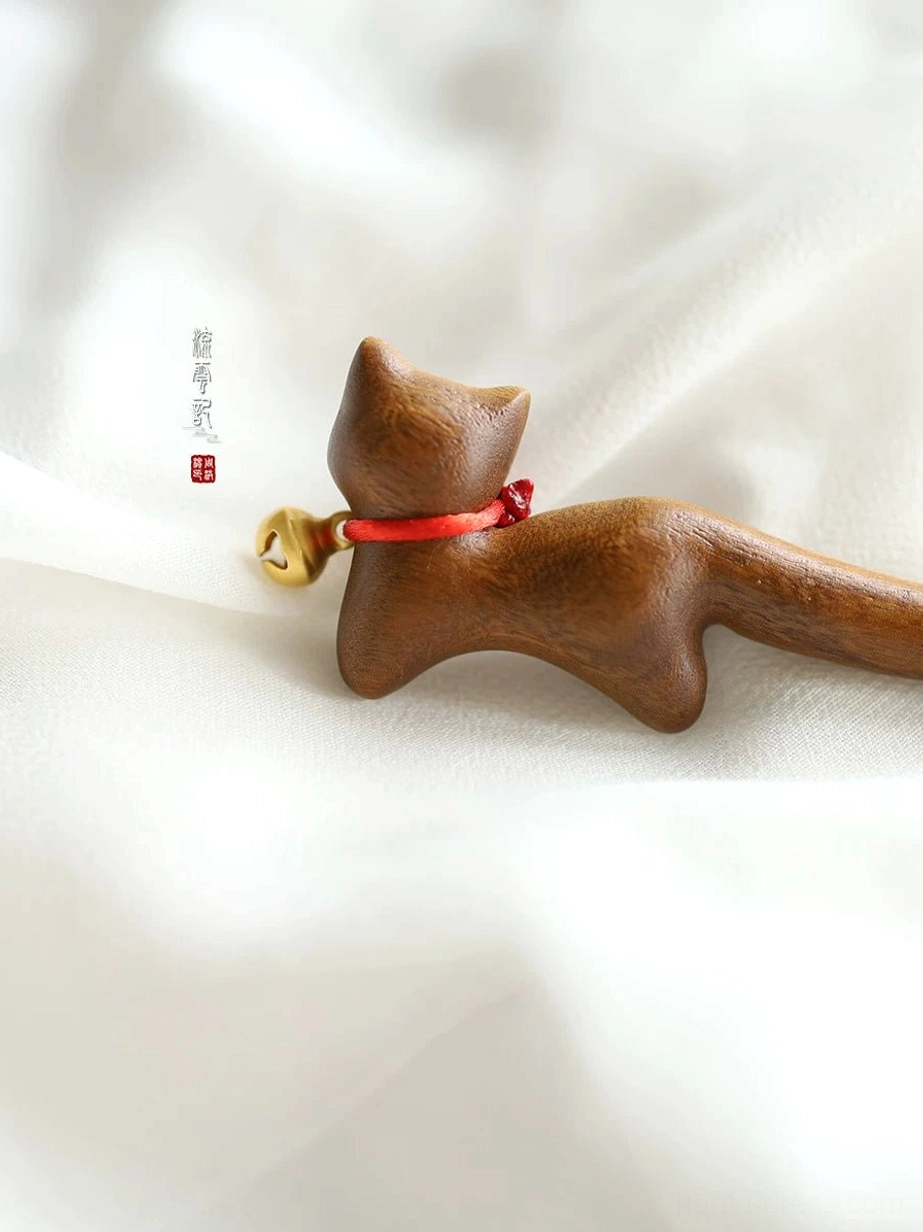Low side view of a lying cat silhouette on a traditional Chinese wooden hair stick, featuring visible wood grain, red collar, and hanging bell