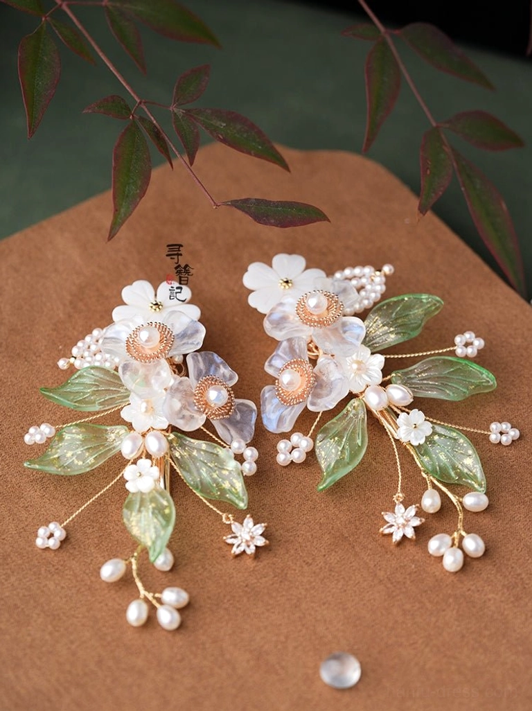 Pair of Magical Bloom Chinese floral hair pins with blue glass flowers green leaves freshwater pearls and gold toned details displayed on a brown leather mat
