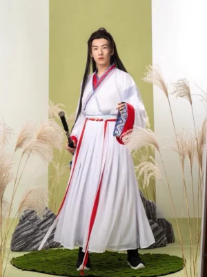 Male hanfu model wearing a white Wei Jin-inspired xianxia outfit with red and blue geometric collar and cuff trim, red sash, pleated skirt, and sword accessory