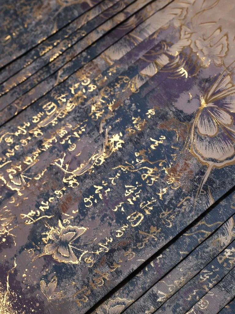 Close up detail of deep blue purple mamianqun pleated fabric with gold traditional Chinese calligraphy, butterfly and floral motifs