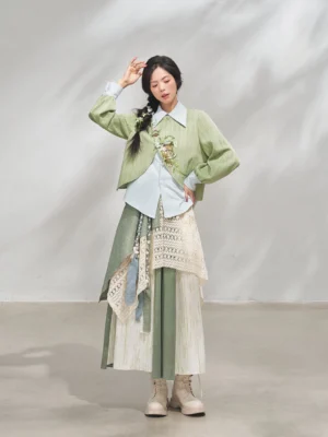 Front full-body view of a woman wearing a matcha green modern Hanfu xianxia outfit with floral embroidered cropped jacket, light blue layered shirt, and irregular patchwork skirt