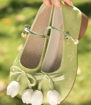 Close-up of matcha green traditional Chinese Hanfu shoes showing white tulip bow decorations, pearl-style ankle strap, woven insole, and low brown block heel